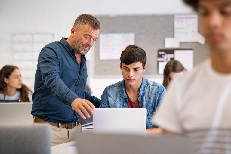 Professor,Assisting,College,Student,With,Laptop,In,Classroom,During,Computer